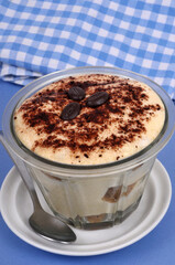 Tiramisu au café dans un ramequin posé sur une soucoupe avec une cuillère en gros plan sur fond bleu