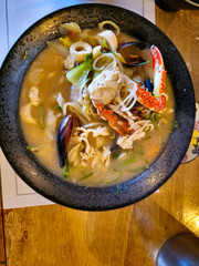 A bowl of soup with a crab on top. The soup is a mix of vegetables and meat