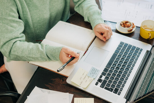 Anonymous woman taking notes while working on laptop