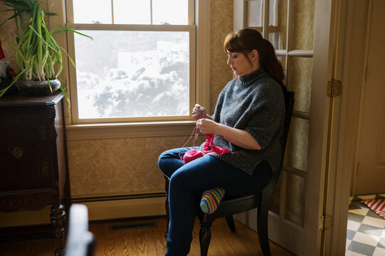 woman sitting down and knitting with hot pink yarn 