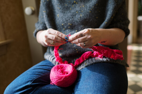 woman sitting down and knitting with hot pink yarn 