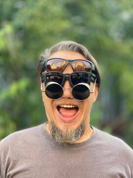 Smiling bearded man wearing four different sunglasses outdoors
