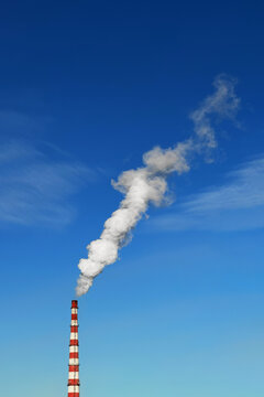 White thick smoke over blue sky coming from industrial chimney