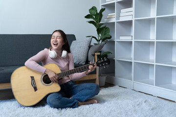 weekend day asian girl is sitting on couch blowing off steam by singing playing guitar at home....