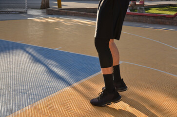 Fototapeta premium a young girl in a black t - shirt and a shorts with a black bag is standing on a basketball court in the city