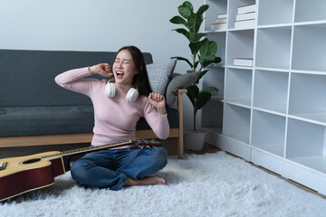 weekend day asian girl is sitting on couch blowing off steam by singing playing guitar at home....