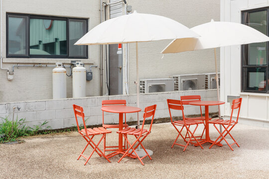 Red tables, chairs and parasols in front of the building.