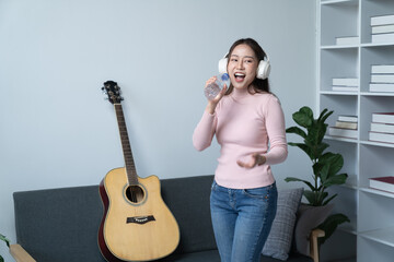 Young singer fun woman wear casual clothes stand near sofa couch using laptop listen music in headphones playing guitar sing song record voice stay home on weekend