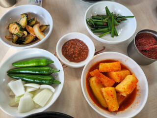 A table with a variety of Asian food, including pickles, peppers, and onions. The table is set for a meal, and the food is arranged in several bowls