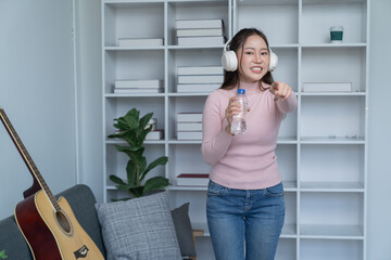 Young singer fun woman wear casual clothes stand near sofa couch using laptop listen music in headphones playing guitar sing song record voice stay home on weekend