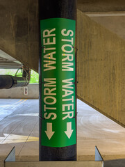 Closeup view of a metal pipe labeled storm water within a concrete parking garage, structure.