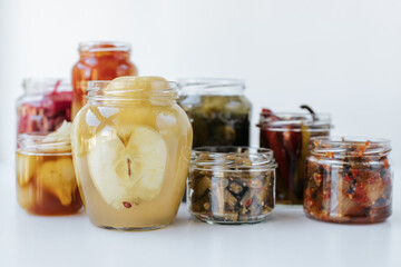 Glass jars of different sizes with fermented vegetables stand on a light background. 