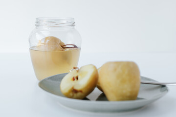 There is a glass jar with a fermented apple on a light background. next to it is a plate with a cut fermented apple and a fork