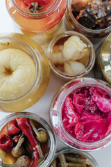 Glass jars of different sizes with fermented vegetables stand on a light background. shot from above