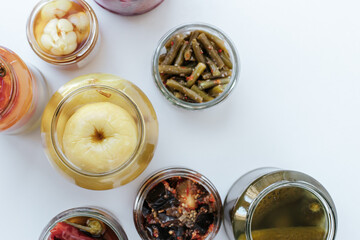 Glass jars of different sizes with fermented vegetables stand on a light background. shot from above