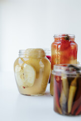 Glass jars of different sizes with fermented vegetables stand on a light background. 