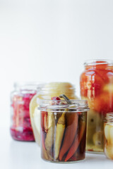 Glass jars of different sizes with fermented vegetables stand on a light background. 