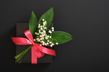 Black gift box with lilies of the valley and pink ribbon on dark background. Space for your text