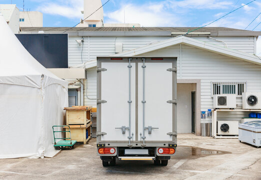 Back door of a box truck parked in front of a white building.