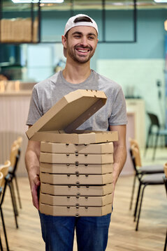 Smiling man is holding a stack of pizza boxes