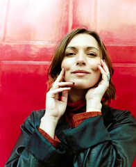 Analogue film portrait of woman posing in front of red door.