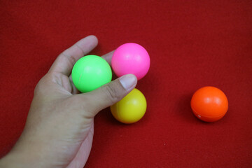 a hand holding Several toy balls are pink, yellow, green and orange on a red background
