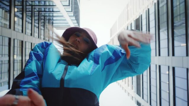 Low angle pov shot hip-hop dance, 80s vintage fashion woman dancing outdoors in modern city downtown high-rise skyscrapers background, creative female dancer moves rhythmically, urban style performer