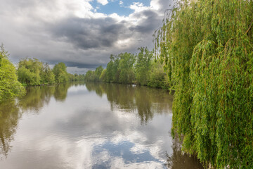 Stormy weather over a tree-lined natural river in spring.