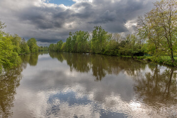 Stormy weather over a tree-lined natural river in spring.