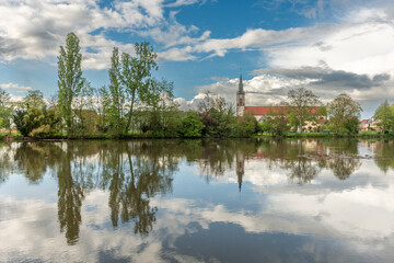 Huttenheim village reflected in a natural tree-lined river in spring.