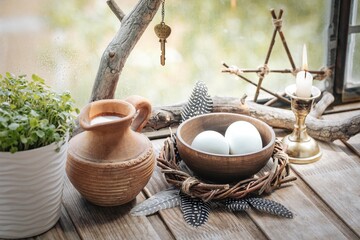 Home atmospheric spring altar with willow wreath, clay jug with milk, bowl with eggs, the first...