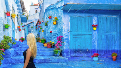 A blonde haired woman in a colourful backstreet with potted plants in Chefchaouen, Morocco.