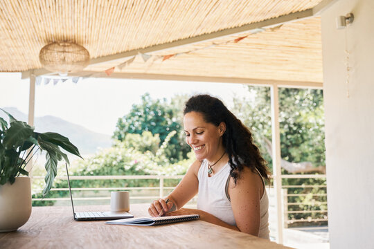 Smiling woman taking notes during remote work at balcony