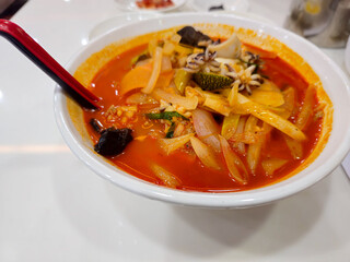 A bowl of red soup with a spoon in it. The soup is full of vegetables and has a spicy taste