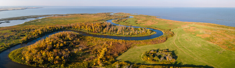 Aerial panoramic view of a large slow moving river that curves through autumn colored farmland and forest before entering a large lake.  
