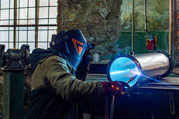 Male welder is welding stainless pipe in industrial workshop