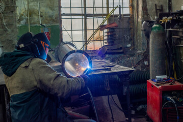 Male welder is welding stainless pipe in industrial workshop