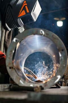 Male welder wearing a protective mask is welding stainless pipe