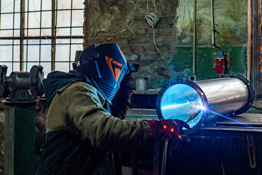 Male welder is welding stainless pipe in industrial workshop