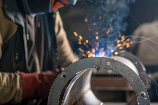 Male welder wearing a protective mask is welding stainless pipe