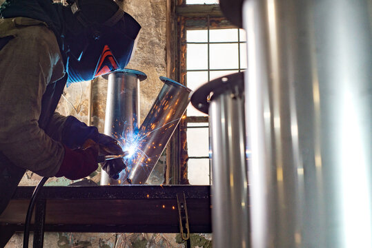 Male welder is welding stainless pipe in industrial workshop