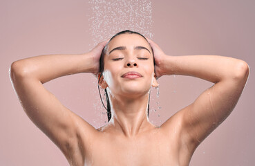 Naklejka premium Woman, hair and shower in studio with water, pink background and relaxing for cleaning or model washing. Grooming, hygiene and female person wet for self care, eyes closed and wellness routine