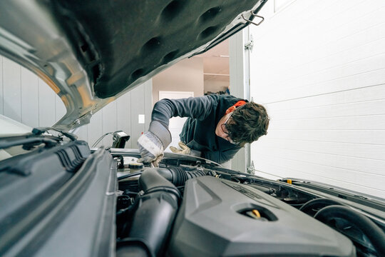 Teen boy doing maintenance on the engine of a car. 