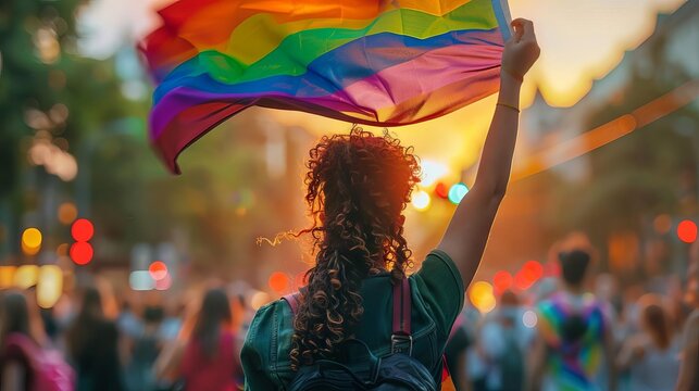 The image shows a person waving a rainbow flag at a pride parade. The flag is a symbol of the LGBTQ+ community, and the parade is a celebration of the diversity of the community.