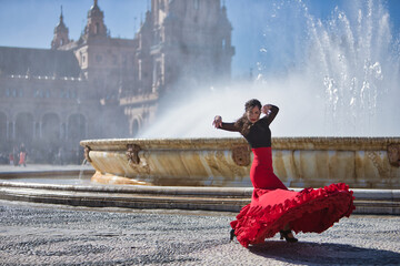 Young, beautiful, brunette woman in black shirt and red skirt, dancing flamenco in front of a...