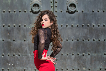 Fototapeta premium Portrait of young, beautiful, brunette woman in black shirt and red skirt, dancing flamenco with old, black metal door in the background. Flamenco concept, dance, art, typical Spanish.