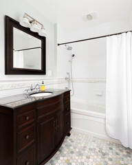 A bathroom with a dark mahogany vanity cabinet, hexagon tile flooring, and a shower with white subway tiles.