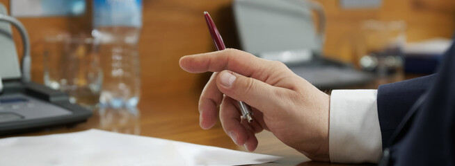 Businessman or official holds a pen while sitting at the table during negotiations or a business...