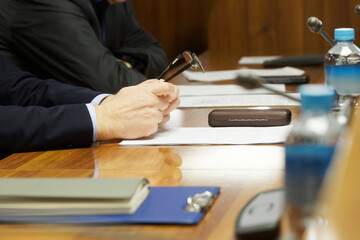 A man in a business suit holds glasses in his hands while studying documents. At the table with colleagues. Businessman, official or lawyer. Selective focus. No face. Photo
