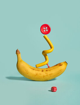 Banana, pushpin, button, hair curler and dice on teal background. 